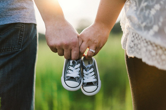 Two people are carrying a pair of baby shoes between them